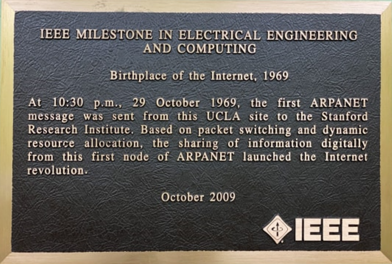 A black commemorative plaque with gold frame, inscribed with gold letters. It reads:
"At 10:30 p.m., 29 October 1969, the first ARPANET message was sent from this UCLA site to the Stanford Research Institute. Based on packet switching and dynamic resource allocation, the sharing of information digitally from this first node of ARPANET launched the Internet revolution."