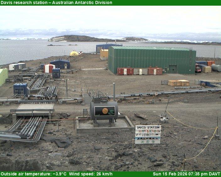 A view of the Davis research station with research buildings, equipment, and vehicles scattered around, and mountains visible in the background. Occasionally features Happy Birthday signs.