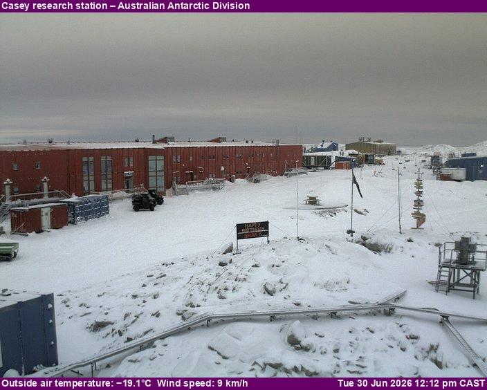 A view of the Casey research station with the main building in the focus and smaller structures and equipment scattered around. Occasionally features Happy Birthday signs.